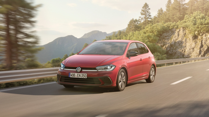 Polo ENERGY fährt dynamisch auf einer Landstraße, Bäume und Felsen im Hintergrund.