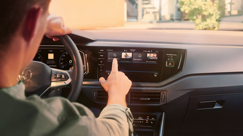 Ein Mann sitzt am Steuer eines VW Polo und bedient das Infotainment-System mit dem Menü der Upgrade-Funktionen.