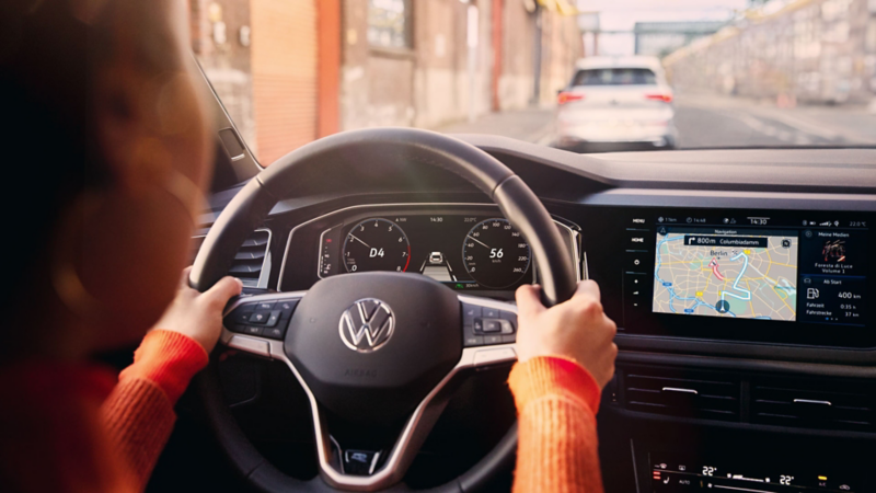 Une femme conduit une VW Polo avec la navigation active affichée sur l’écran du système d’infodivertissement.