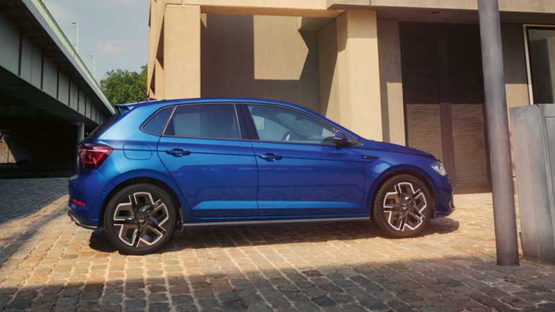 Ein blauer VW Polo in Seitenansicht parkt vor einem Hochhaus.