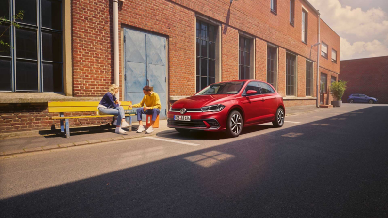Zwei Personen spielen Schach vor einem roten VW Polo Style, der vor einem Fabrikgebäude parkt.