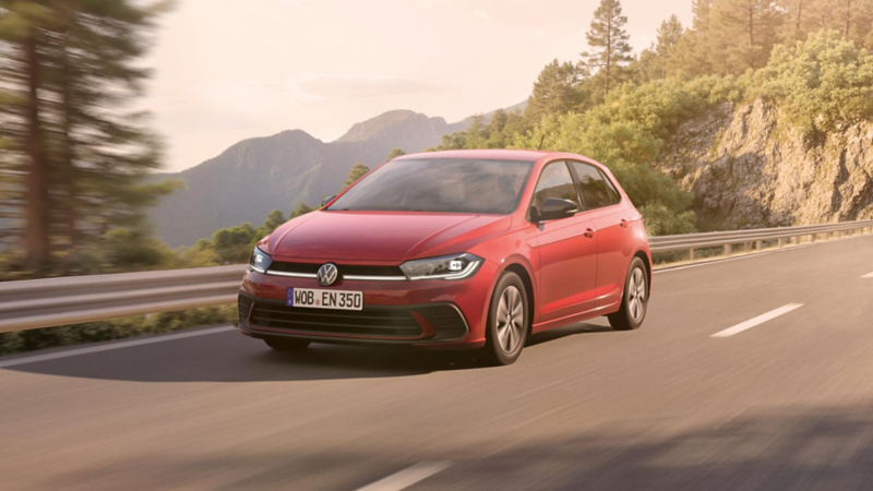 Polo ENERGY fährt dynamisch auf einer Landstraße, Bäume und Felsen im Hintergrund.