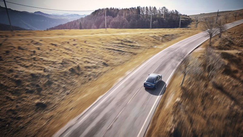 Ein blauer VW ID.7 fährt bei Sonnenschein auf einer Landstraße.