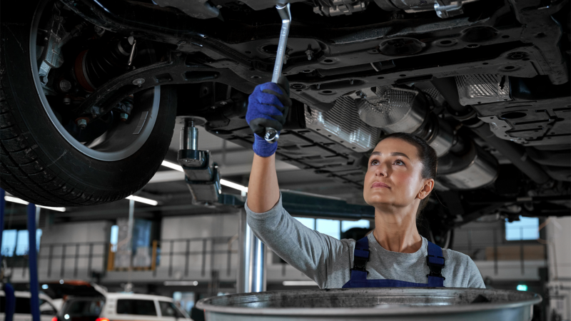 Technicien VW effectuant l’entretien sous un véhicule Volkswagen.