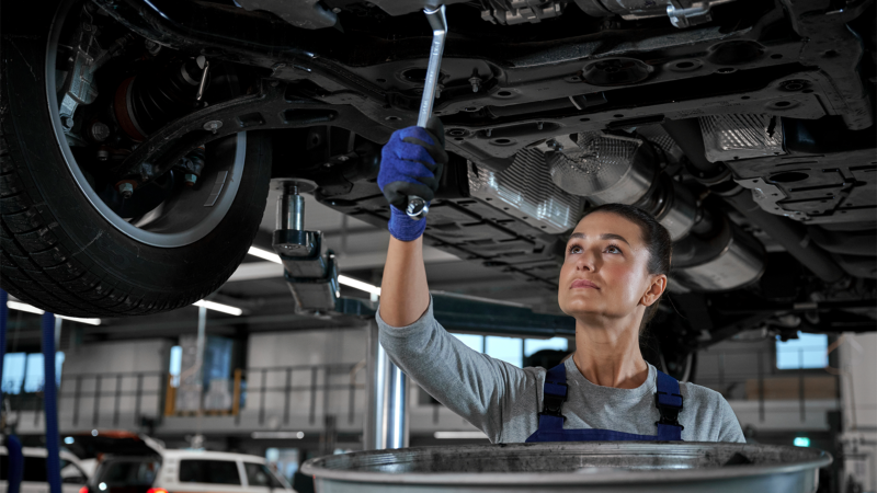 Technicien VW effectuant l’entretien sous un véhicule Volkswagen.