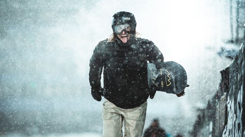 Pat Burgener geht mit seinem Snowboard in der Hand einen Berg hoch