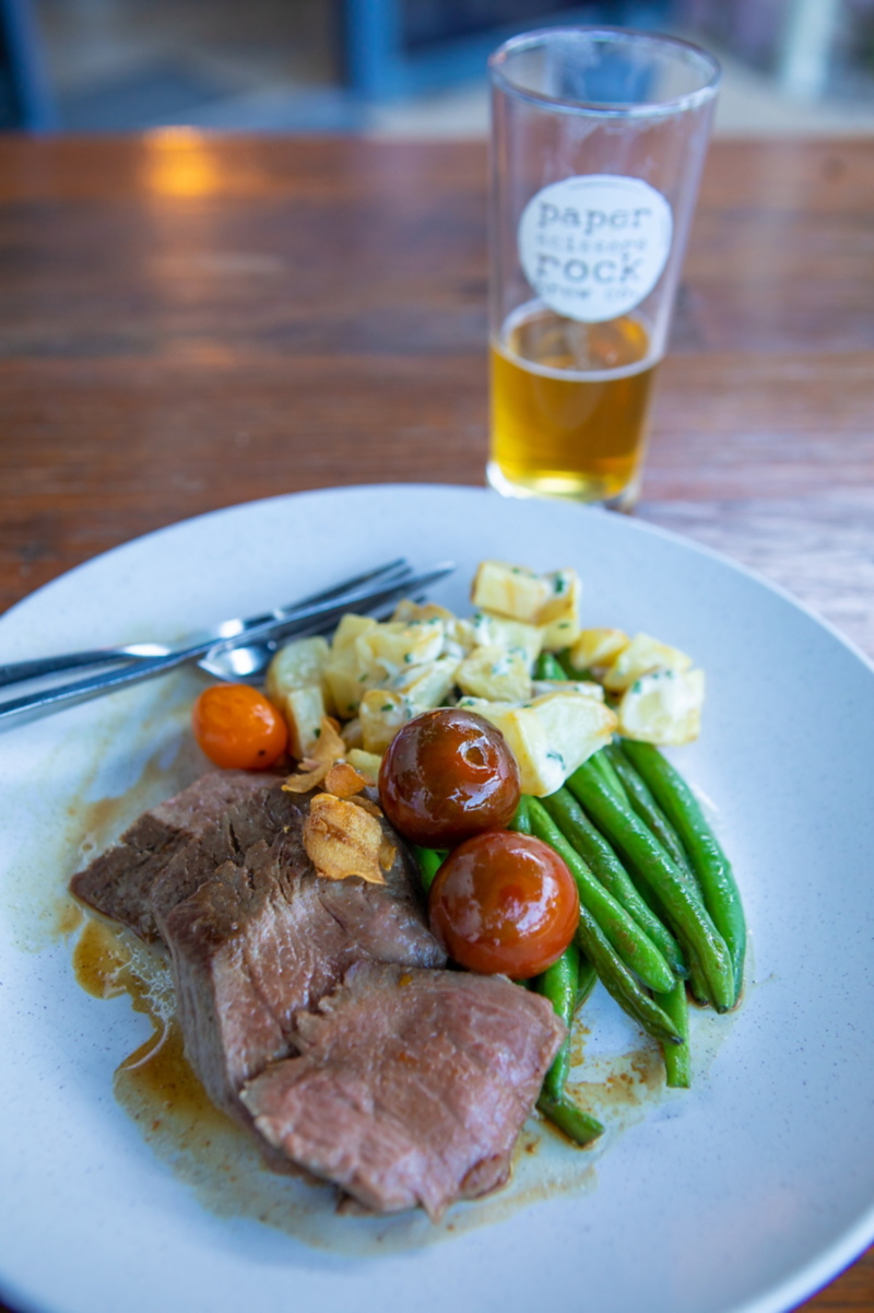 Close up photo of meal including meat and vegetables and pint of beer