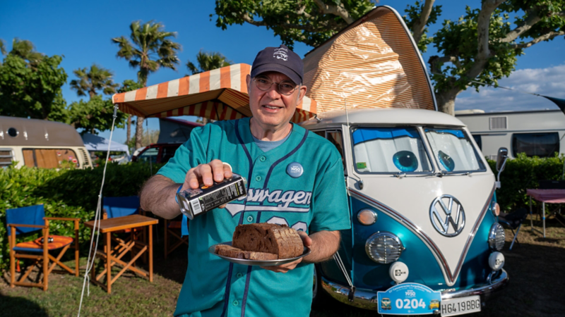 Un hombre de pie sujetando un plato de comida delante de una VW T1.