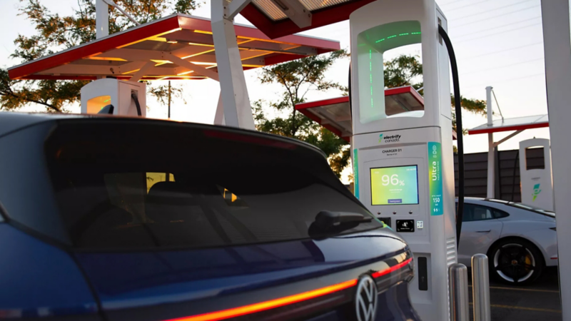 A rear view of a blue Volkswagen ID.4 electric car being charged at an Electrify Canada charging station with its screen displaying 96% indicating the battery level.