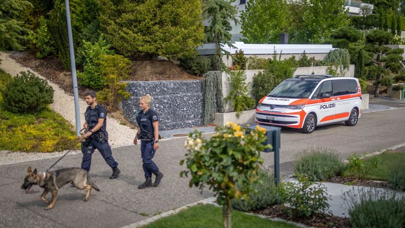 Zwei Polizisten laufen mit dem Polizeihund vom Multivan eHybrid weg Multivan eHybrid