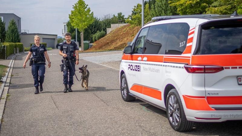 Der Multivan eHybrid steht auf der Strasse, während die Polizisten mit dem Polizeihund auf ihn zulaufen