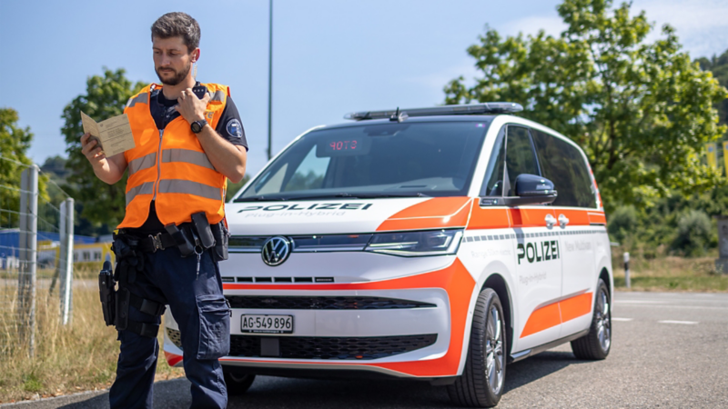 L'agente di polizia Dewis Fuss si trova davanti al multivan della polizia e guarda i documenti del veicolo.
