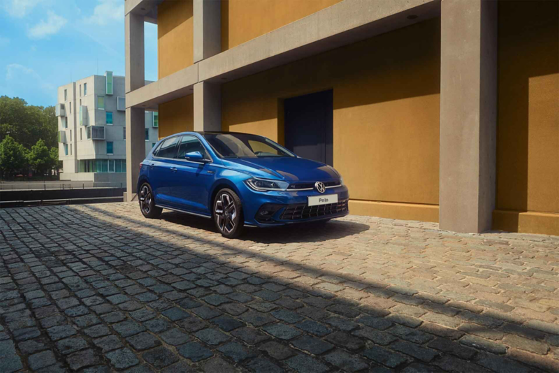Una Polo R-Line parcheggiata sul selciato accanto a un edificio. Vista della parte anteriore e del lato passeggero.