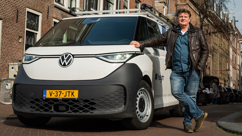 Een man leunt tegen een witte elektrische Volkswagen ID. Buzz Cargo van Heym in een binnenstad.