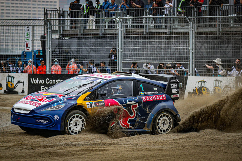En rallybil kör så att sanden sprutar bakom bilen på en bana