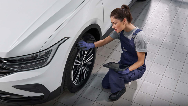 Mecánica de servicio Volkswagen inspecciona neumáticos de Tiguan 2026 blanco con tablet para registro digital.