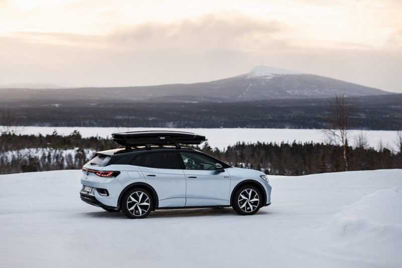 Volkswagen ID.4 kör på en snötäckt landsväg omgiven av skog och fjäll i bakgrund