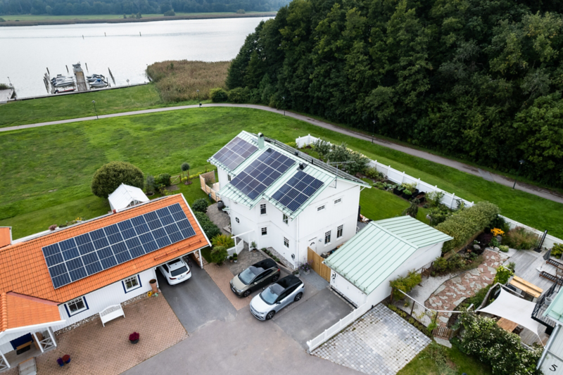 En tomt med hus som har solceller, på gårdsplan står två Volkswagen parkerade