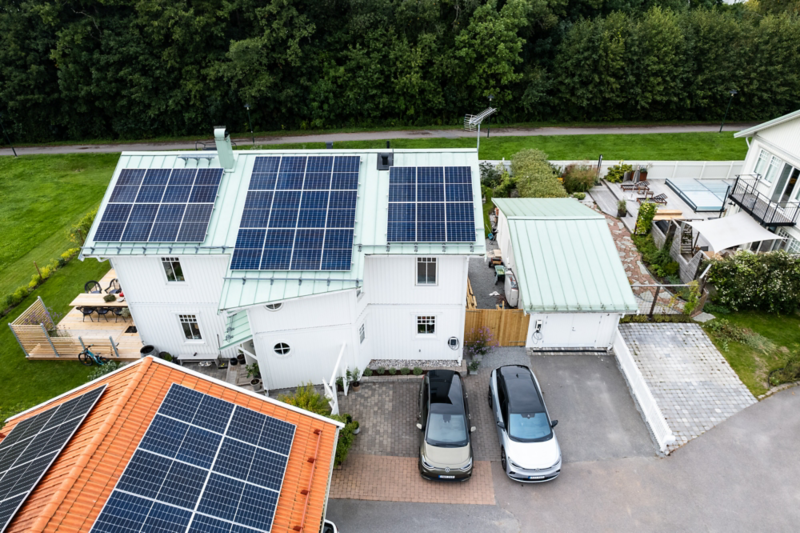 En tomt med hus som har solceller, på gårdsplan står två Volkswagen parkerade