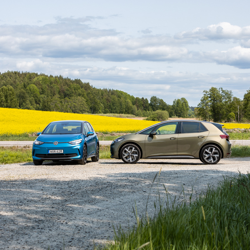 En blå och en grön VW ID.3 står parkerade på en väg med gula rapsfält i bakgrunden