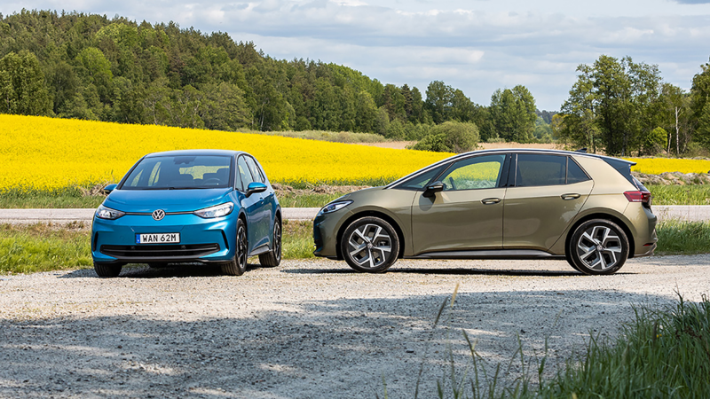 En blå och en grön VW ID.3 står parkerade på en väg med gula rapsfält i bakgrunden