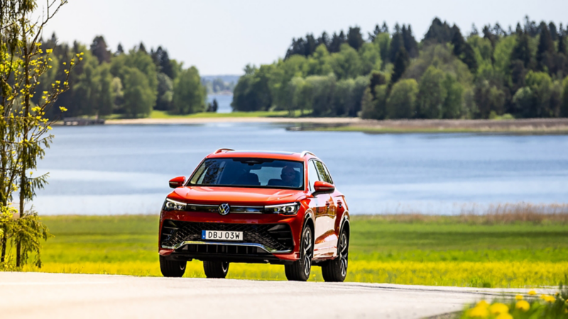 En röd Volkswagen SUV kör längs en väg med havet i bakgrunden
