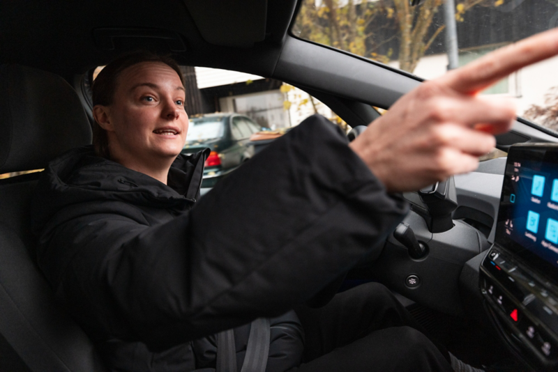 Daniella sitter i förarsätet på ID.3 och pekar ut genom fönstret