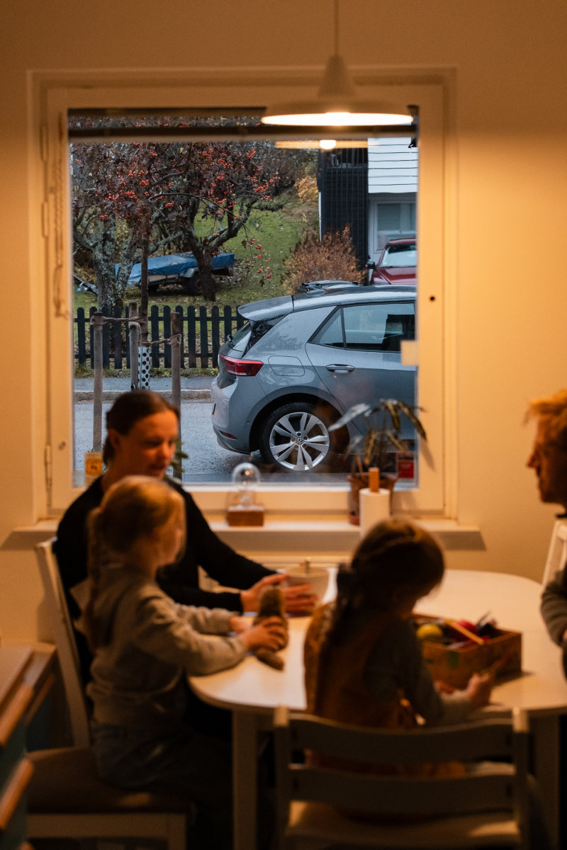 En familj sitter vid matbordet, utanför fönstret står en Volkswagen ID.3 parkerad
