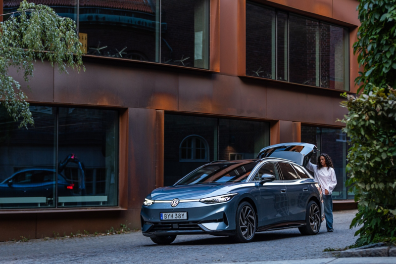 Blå Volkswagen står parkerad vid en byggnad med bagageluckan som öppnas av en person.