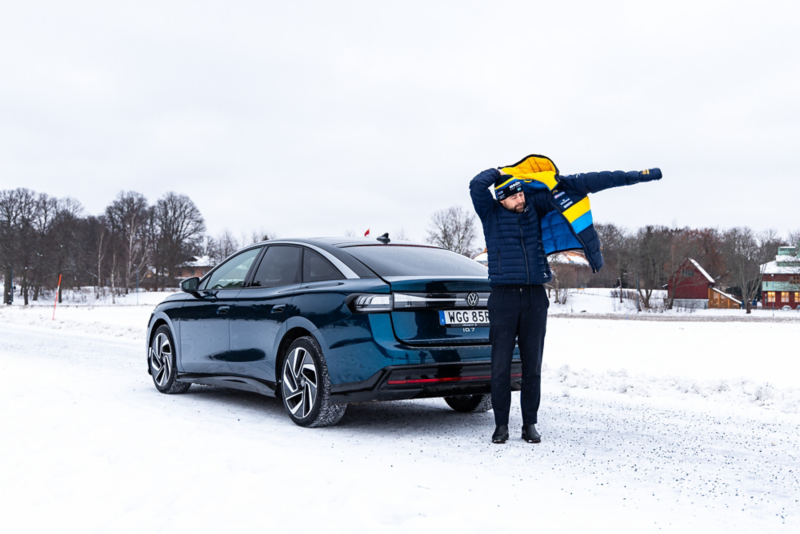 Rikard Grip tar på sig jackan bakom Volkswangen ID.7 som står parkerad längs vägen.