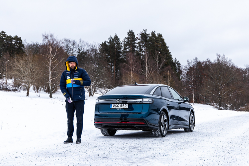 Rikard Grip drar upp dragkedjan på jackan. I bakgrunden står Volkswagen ID.7.