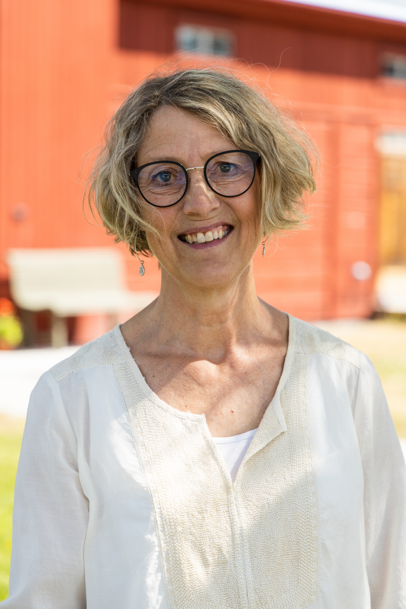 Porträttbild av Elisabet Engelbrekts med ett rött trähus i bakgrunden