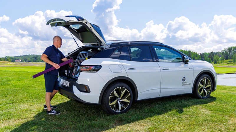 Vit Volkswagen ID.4 sedd från sidan, parkerad på en golfbana medan Henrik lastar in bagage