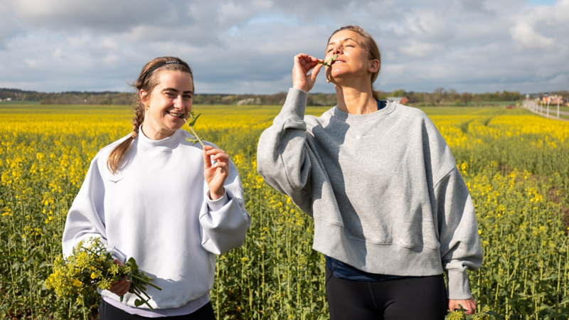 Ebba andersson och Tina Nordström äter rapsblommor, gult rapsfält i bakgrunden