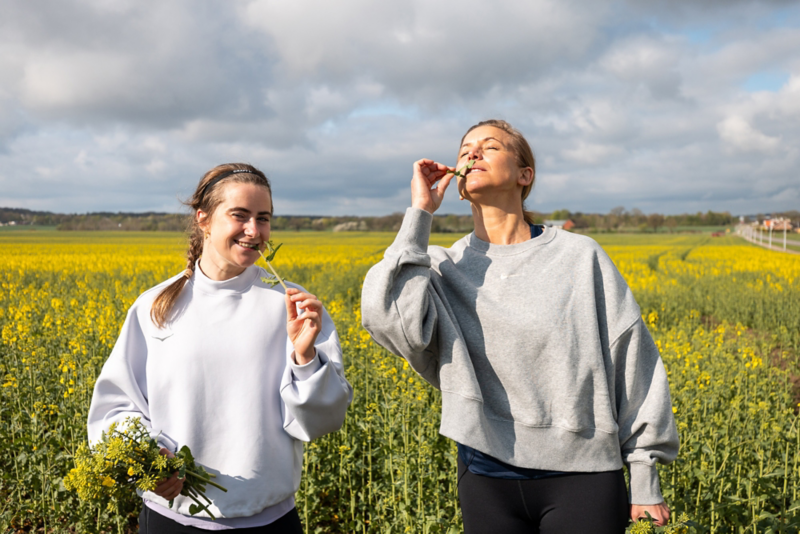 Ebba andersson och Tina Nordström äter rapsblommor, gult rapsfält i bakgrunden