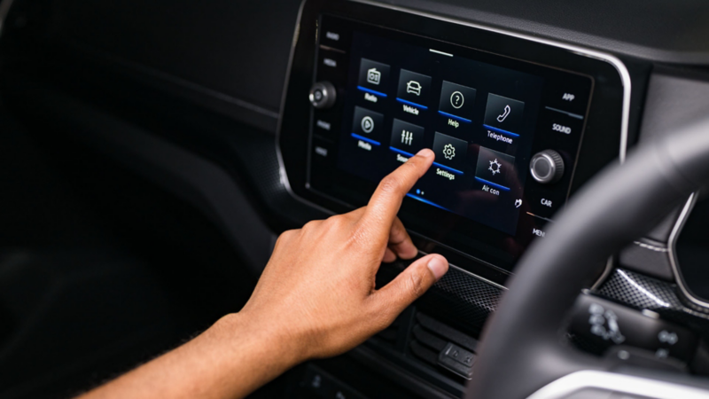 A young woman operates the radio from the driver’s seat via the large display of the infotainment system.