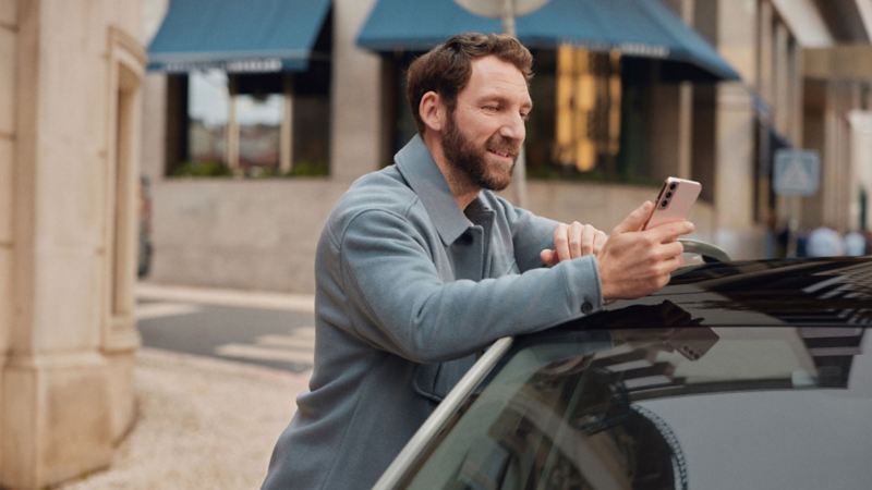 A person leaning on a Volkswagen ID. holding a smartphone in their hand