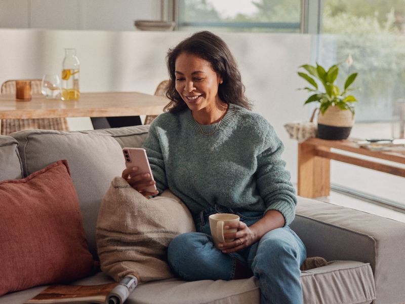 Una donna consulta il suo smartphone mentre è seduta sul divano in casa