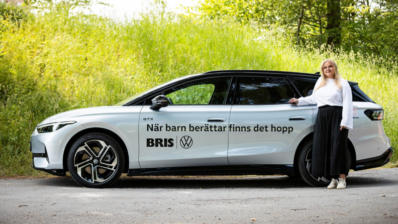 Bris kurator Jennifer Pettersson står bredvid en Volkswagen ID.7 Turer med budskapet "när barn berättar finns det hopp" skrivet på bilenBris kurator Jennifer Pettersson står bredvid en Volkswagen ID.7 Turer med budskapet "när barn berättar finns det hopp" skrivet på bilen