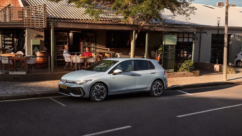 Volkswagen Golf R-Line de couleur grise, garée dans une rue avec des cafés en arrière-plan. 