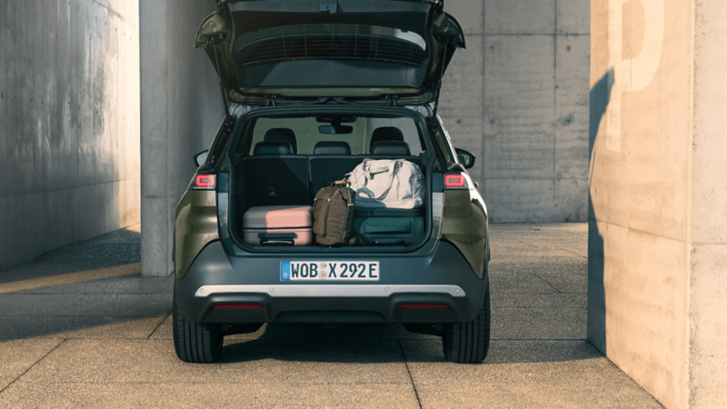 Back view of a VW ID. Cross with its boot opened containing 2 small suitcases, a backpack and a small holdall bag.