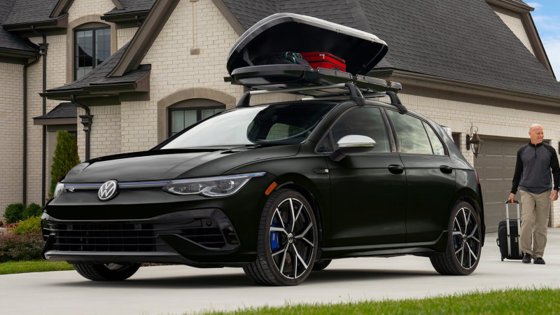 Volkswagen Jetta with open cargo box and an owner rolling his suit case towards the vehicle.