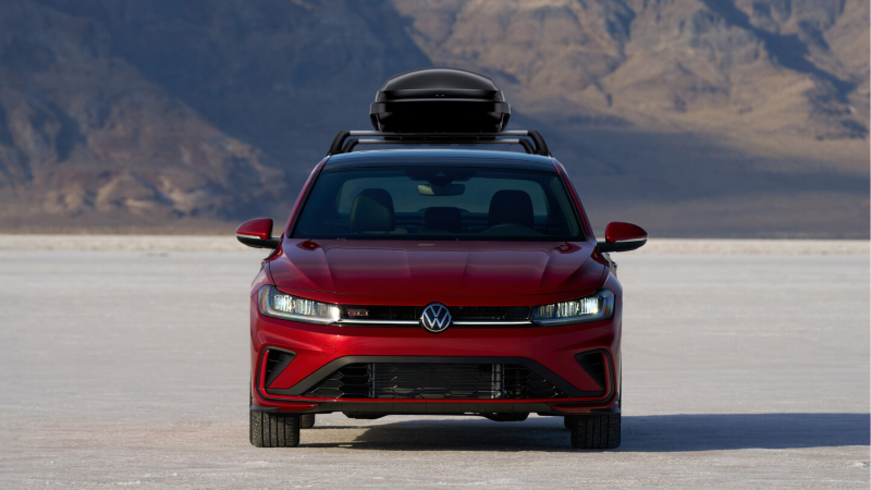Volkswagen Jetta with open cargo box and an owner rolling his suit case towards the vehicle.