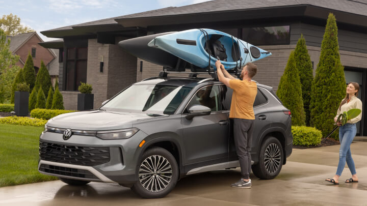 An owner adding a kayak to the roof rack of a Volkswagen Tiguan.