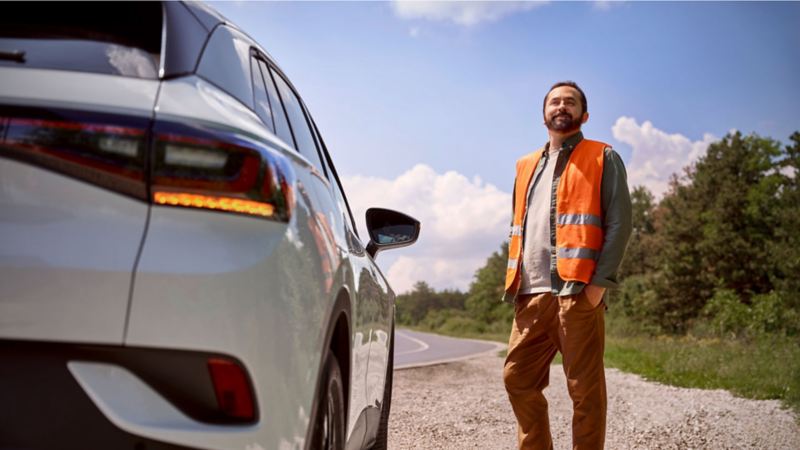 Man in orange VW vest standing next to Volkswagen vehicle.