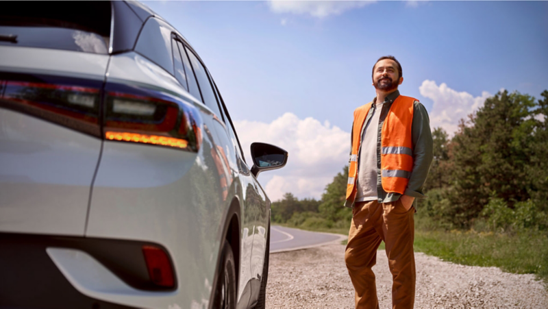 Hombre con chaleco naranja de VW de pie junto al vehículo Volkswagen.