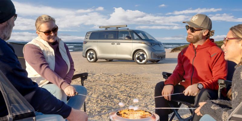 People sitting on beach in front VW ID. Buzz.