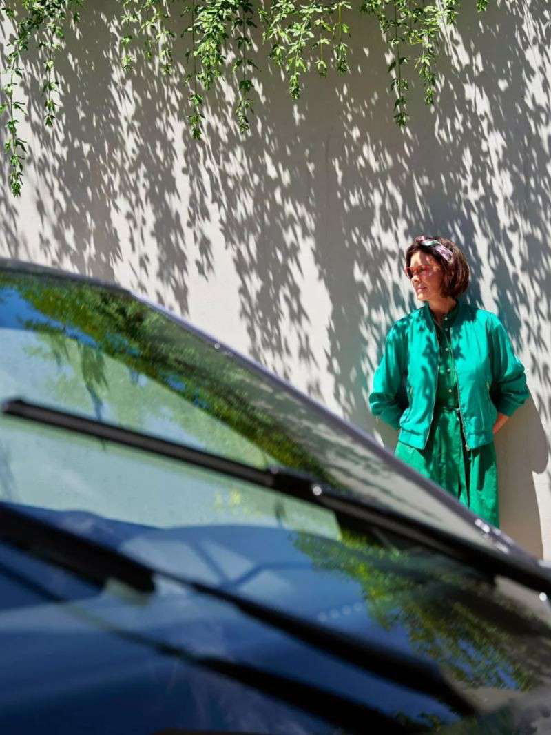 Mujer con vestido verde de pie junto a su vehículo Volkswagen estacionado.
