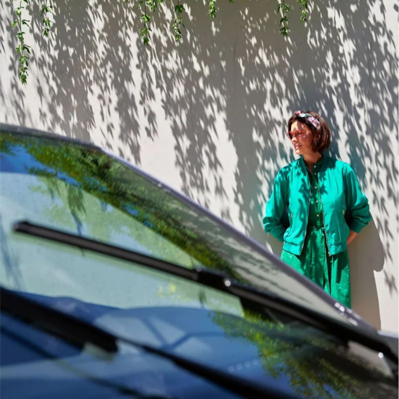 Woman in green dress standing beside her stationary Volkswagen vehicle.