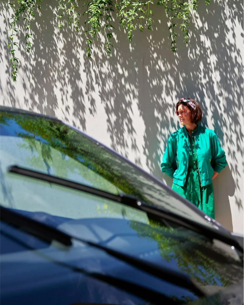 Woman in green dress standing beside her stationary Volkswagen vehicle.